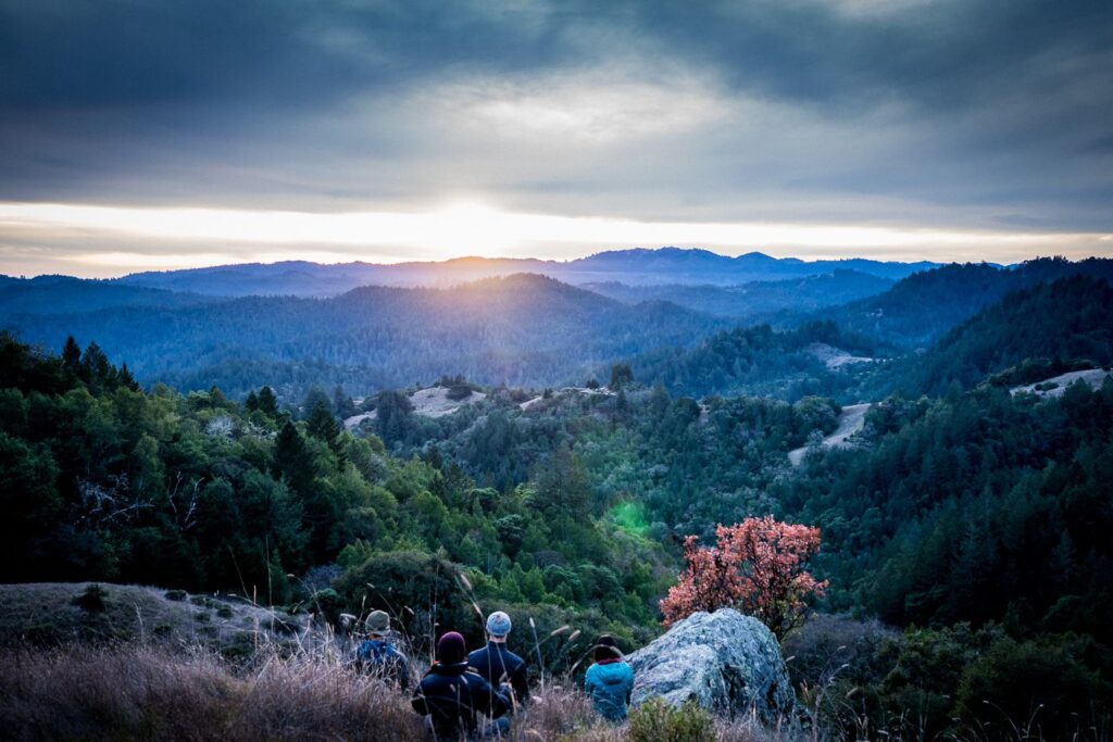 Small group hiking above a forested valley at sunset
